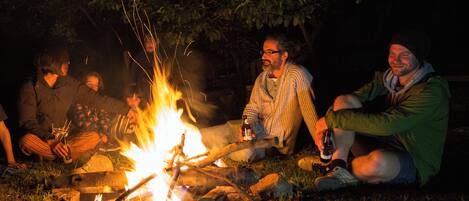 A group of people sitting around a campfire outdoors at night.