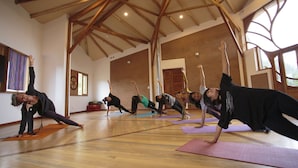 A spacious room with wooden beams on the ceiling, large windows, and a group of people doing yoga on mats. - Fleur Lodge (Acopampa)