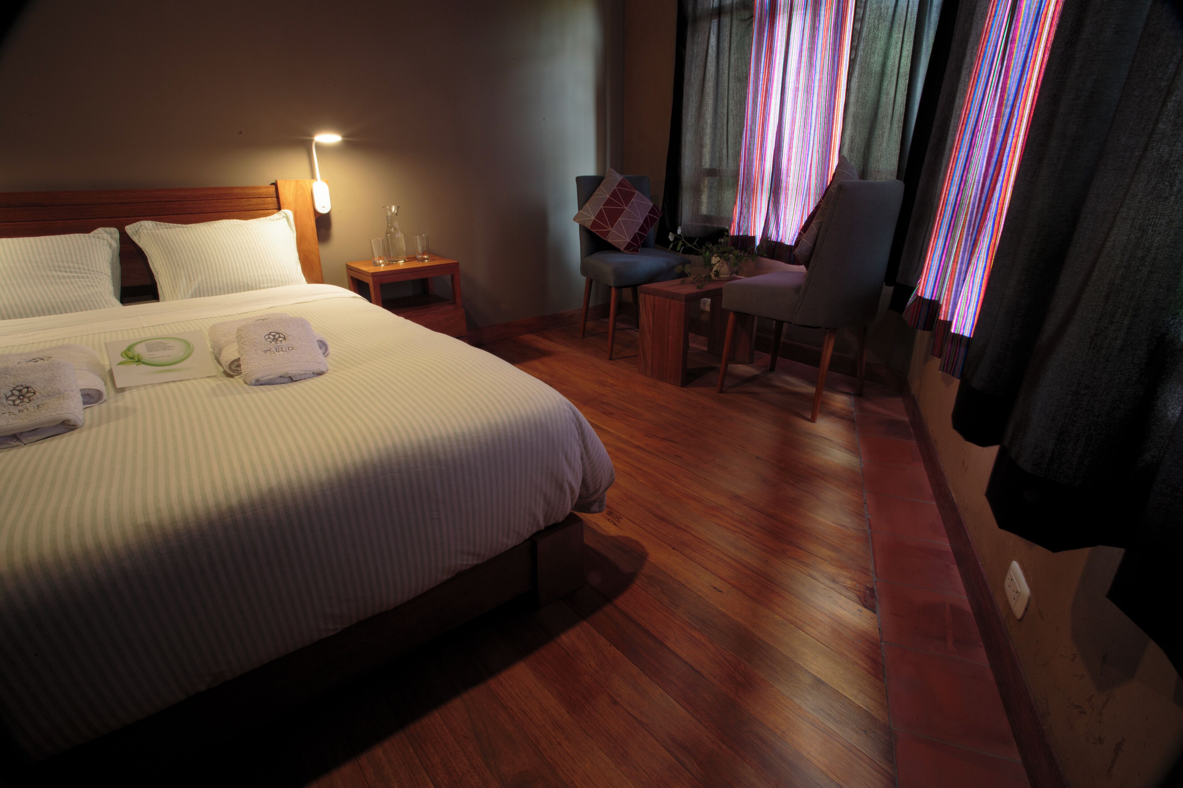 A hotel room with a large bed, a small table, a chair, and a window with curtains.