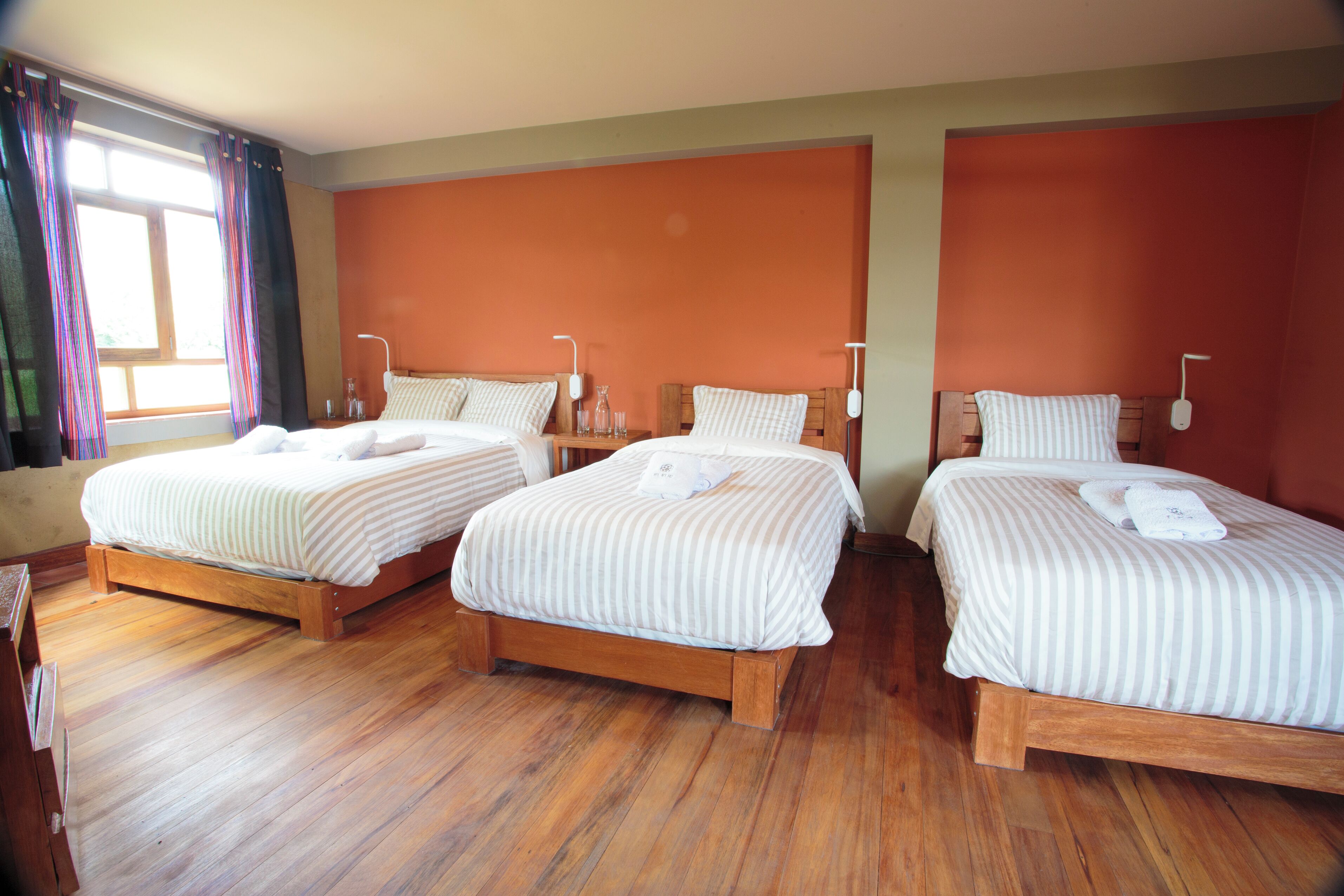 A hotel room with two single beds, wooden flooring, and orange walls.