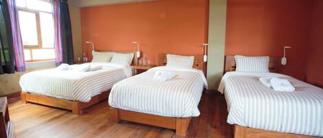 A hotel room with two single beds, wooden flooring, and orange walls.