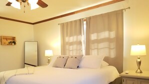 Een hotelkamer met een groot bed, twee bedlampen, een nachtkastje, een houten hoofdbord, een plafondventilator en een raam met gordijnen.