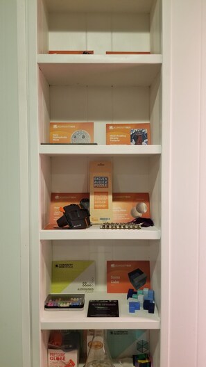 A shelf with various puzzles and games, including a hydroptic maze, a mind-reading miracle tentacle, a baguen audier puzzle, and a soma cube.
