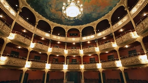 Un teatro sontuoso con balconate decorate, un lampadario e un palcoscenico centrale.