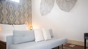 Un dormitorio moderno con un sofá azul claro, un papel tapiz estampado y una gran obra de arte con hojas en la pared.