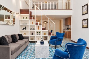 A modern living room with a sofa, blue chairs, a coffee table, and a staircase leading to a kitchen.