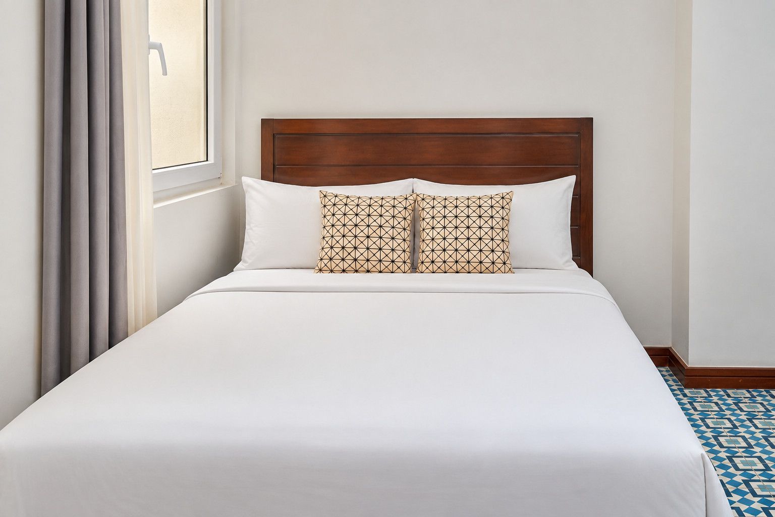 Une chambre d’hôtel avec un lit, une fenêtre avec des rideaux et un sol à motifs.