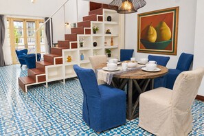 A dining area with a round table set for four, surrounded by blue and beige chairs. A staircase with wooden steps and white shelves is visible in the background. - - (Ciudad de Panamá)