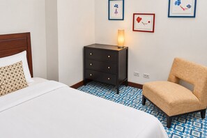 A hotel room with a bed, a nightstand, a chair, and a wall with framed artwork.