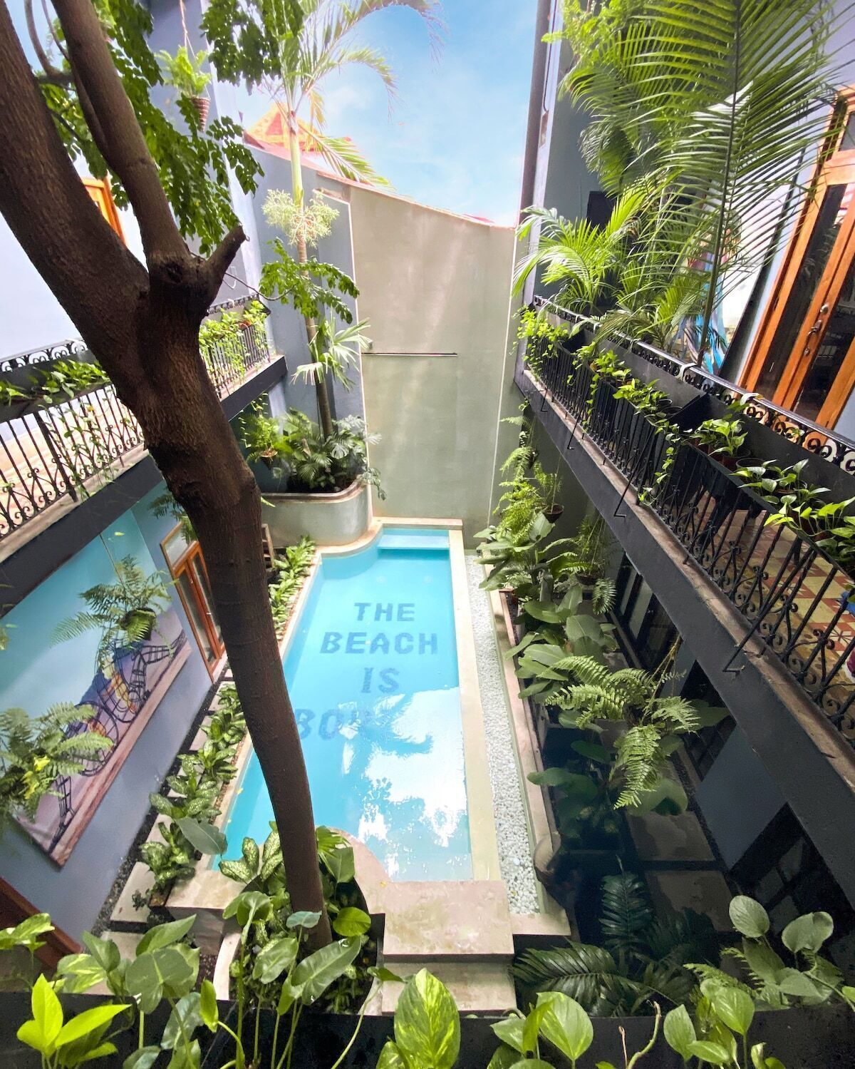 Una piscina interior pequeña rodeada de abundante vegetación y un mural que representa una playa.