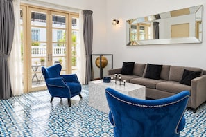 Una habitación con una silla azul, un sofá, una mesa de centro y un espejo grande en la pared.
