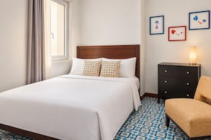 Una habitación de hotel con una cama grande, un aparador, una silla y una mesita de noche con lámpara.