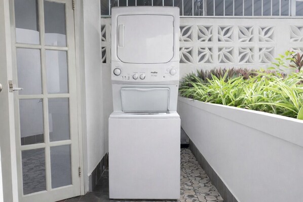 A compact, white laundry room with a built-in washer and dryer, a door with frosted glass panels, and a decorative white wall with geometric patterns.