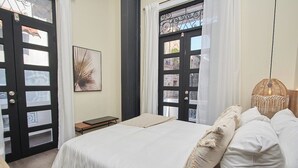 A bedroom with a large bed, a small bedside table, a wall-mounted picture, and a window with curtains. - Outstanding double appartment with pool and rooftop (Ciudad de Panamá)
