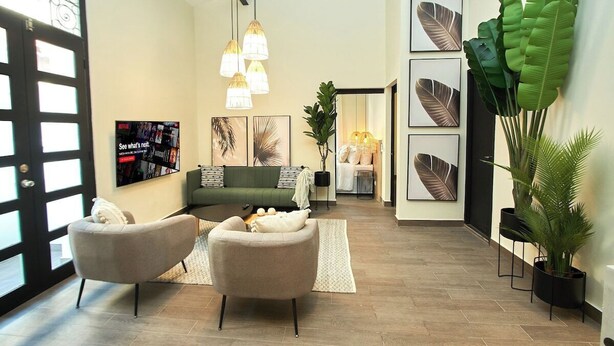 A modern living room with a green sofa, two armchairs, and a coffee table. There are framed artworks on the walls, a large plant, and a TV displaying a Netflix advertisement. - Outstanding double appartment with pool and rooftop (Ciudad de Panamá)