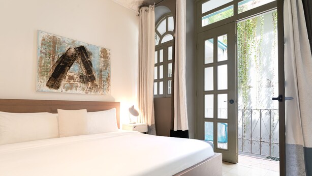 A hotel room with a large bed, a painting on the wall, a window with curtains, and a view of the outside.