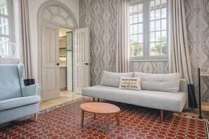 A living room with a light blue armchair, a grey sofa with a cushion, a small round wooden table, and a patterned red and white floor.