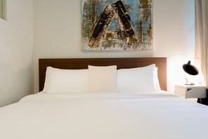 A neatly made bed with white linens, a wooden headboard, and a single bedside table with a lamp.