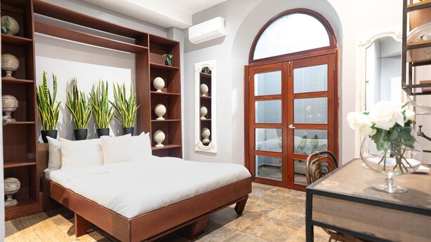 A bedroom with a large bed, built-in shelving, a wooden door, and a dining table with a vase of flowers. - Apartment with 3 Double Bedrooms / 3 Bathrooms M0 (Ciudad de Panamá)