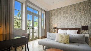 A hotel room with a bed, a desk, and a chair. There is a window with curtains, a patterned wall, and a lamp on the bedside table. - Spacious Apartment in Casco Viejo with Terrace M5 (Ciudad de Panamá)