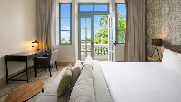 A hotel room with a bed, a desk, a chair, a small table, and a balcony with curtains. - Spacious Apartment in Casco Viejo with Terrace M5 (Ciudad de Panamá)