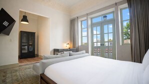 A hotel room with a large bed, a desk with a lamp, a wardrobe, and a view of the outside through large windows. - Spacious Apartment in Casco Viejo with Terrace M5 (Ciudad de Panamá)