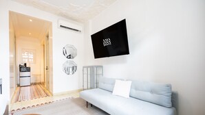 Una sala de estar moderna con un sofá azul claro, un televisor de pantalla plana montado en la pared y una alfombra estampada en el suelo.