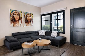 A modern living room with a sectional sofa, two round wooden tables, a large window, and a dark door.