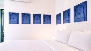 Ein Hotelzimmer mit einem großen Bett, weißer Bettwäsche und sechs blauen Wandbildern.