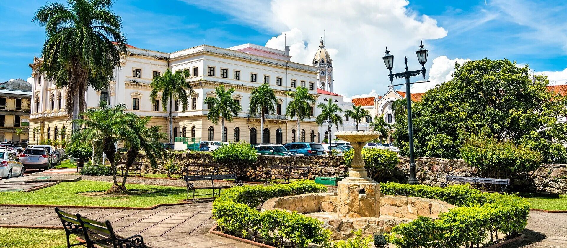 Un edificio histórico con una fuente, palmeras y cielo despejado.