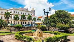 A historic building with a fountain, palm trees, and a clear sky.
