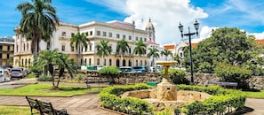 A historic building with a fountain, palm trees, and a clear sky.