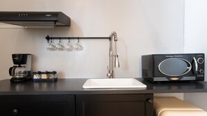 Eine Küche mit schwarzem Arbeitsplatz, einer weißen Spüle, einer schwarzen Mikrowelle und einer Kaffeemaschine.