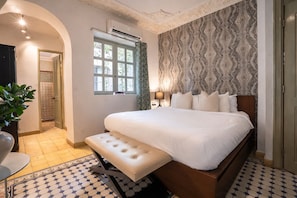 Un dormitorio con una cama grande, un banco, una ventana y papel tapiz estampado.