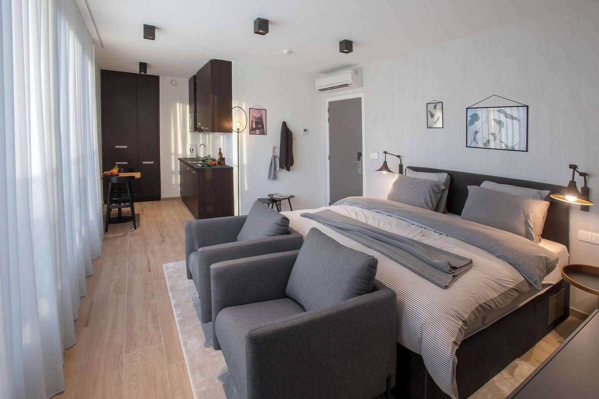 Ein modernes Schlafzimmer mit einem gro ßen Bett, zwei Sesseln, einem kleinen Tisch und einer Küchenzeile.