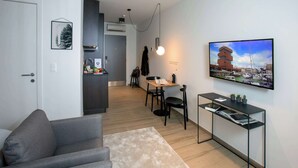 A modern living room with a grey sofa, a small table with a lamp, a TV mounted on the wall, and a view of a marina. - Q-Stay (Antwerp)