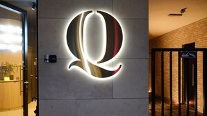 A hotel entrance with a large illuminated letter 'Q' on the wall, a reception desk, and a gated entrance. - Q-Stay (Antwerp)