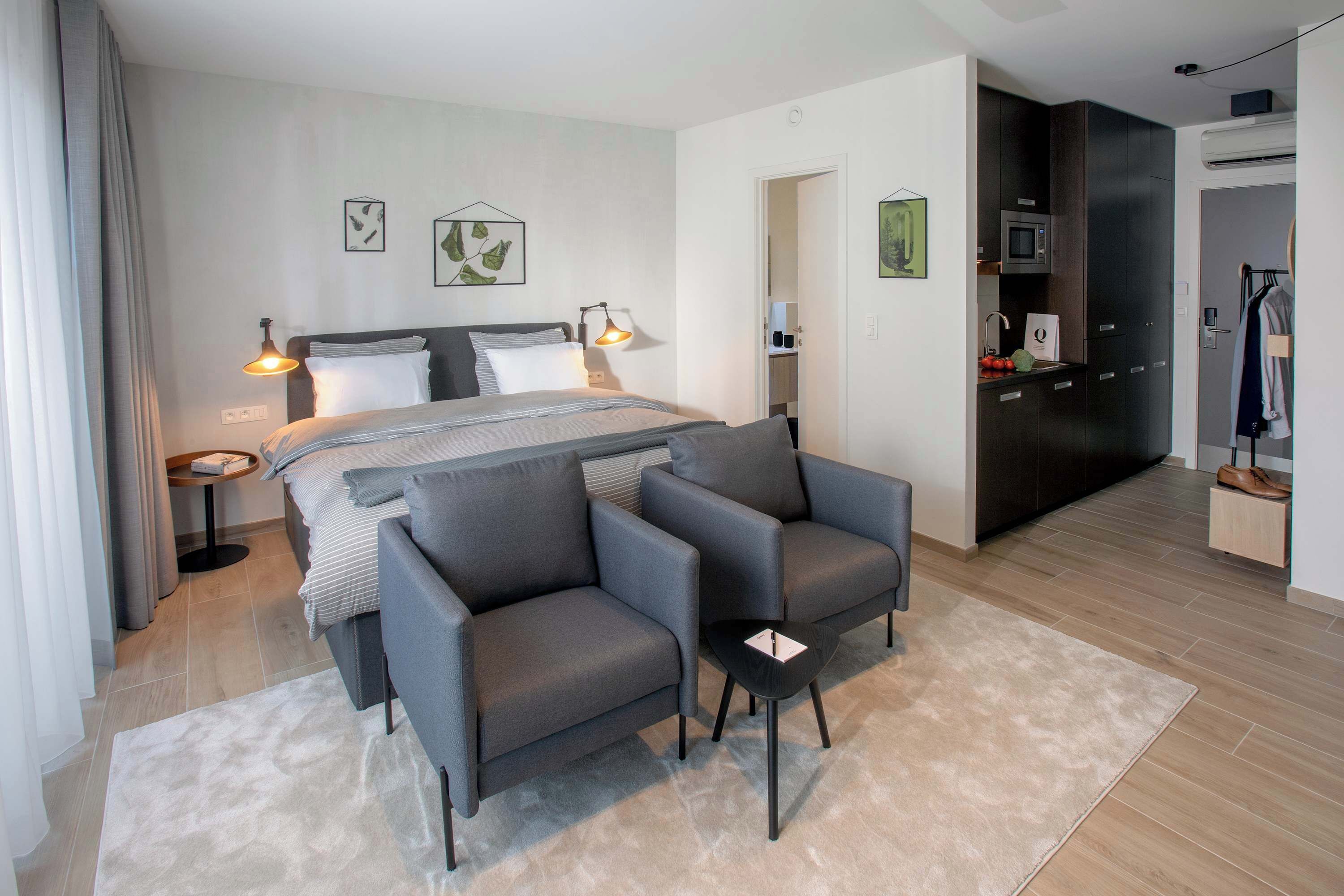 Una habitación de hotel moderna con una cama, dos sillones, una mesita, un escritorio y un armario.