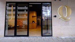 A hotel entrance with a large illuminated 'Q' sign, a reception desk, and a view of the interior through the glass doors. - Q-Stay (Antwerp)