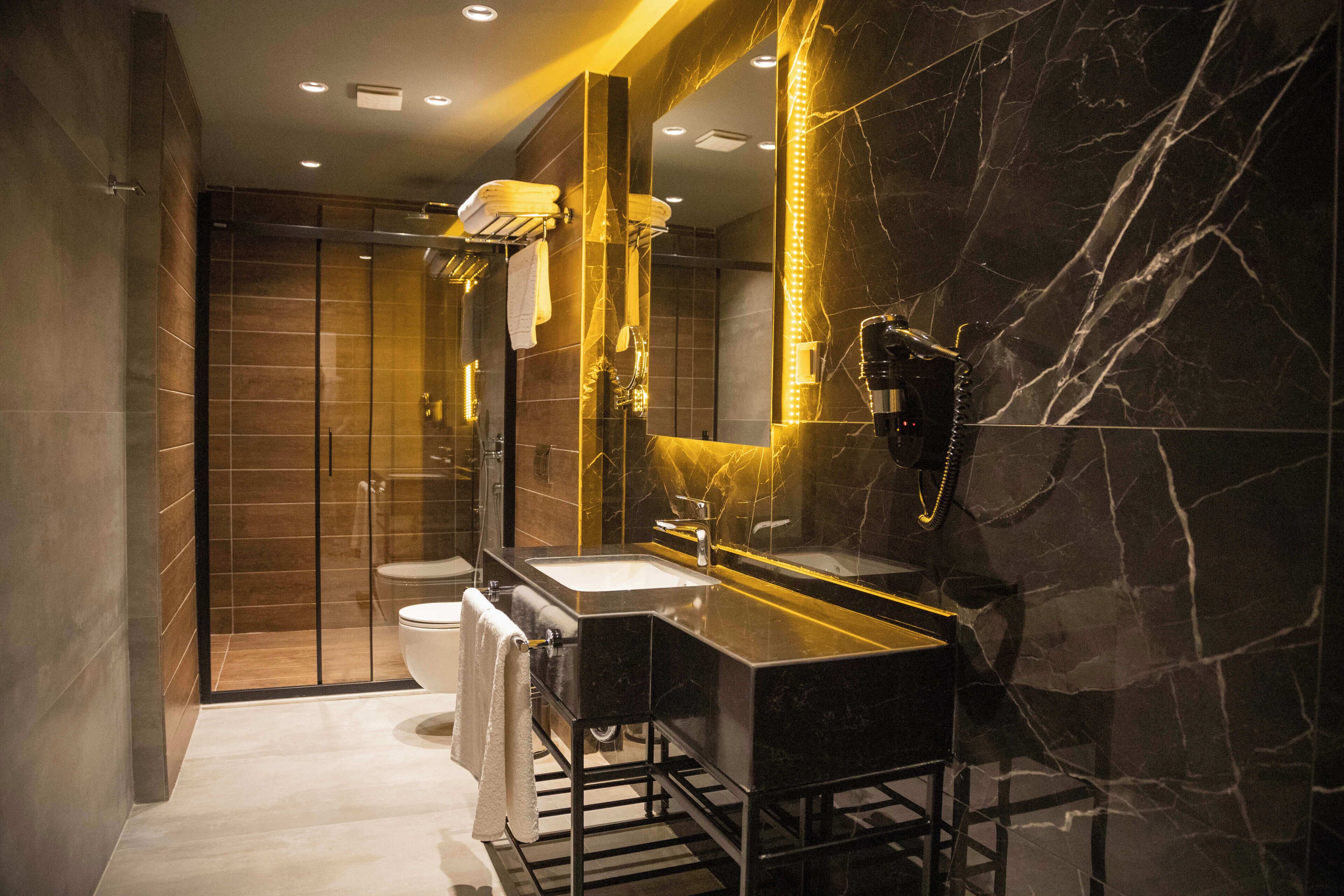 A modern bathroom with a black marble sink, a glass-enclosed shower, and a large mirror with a vanity.