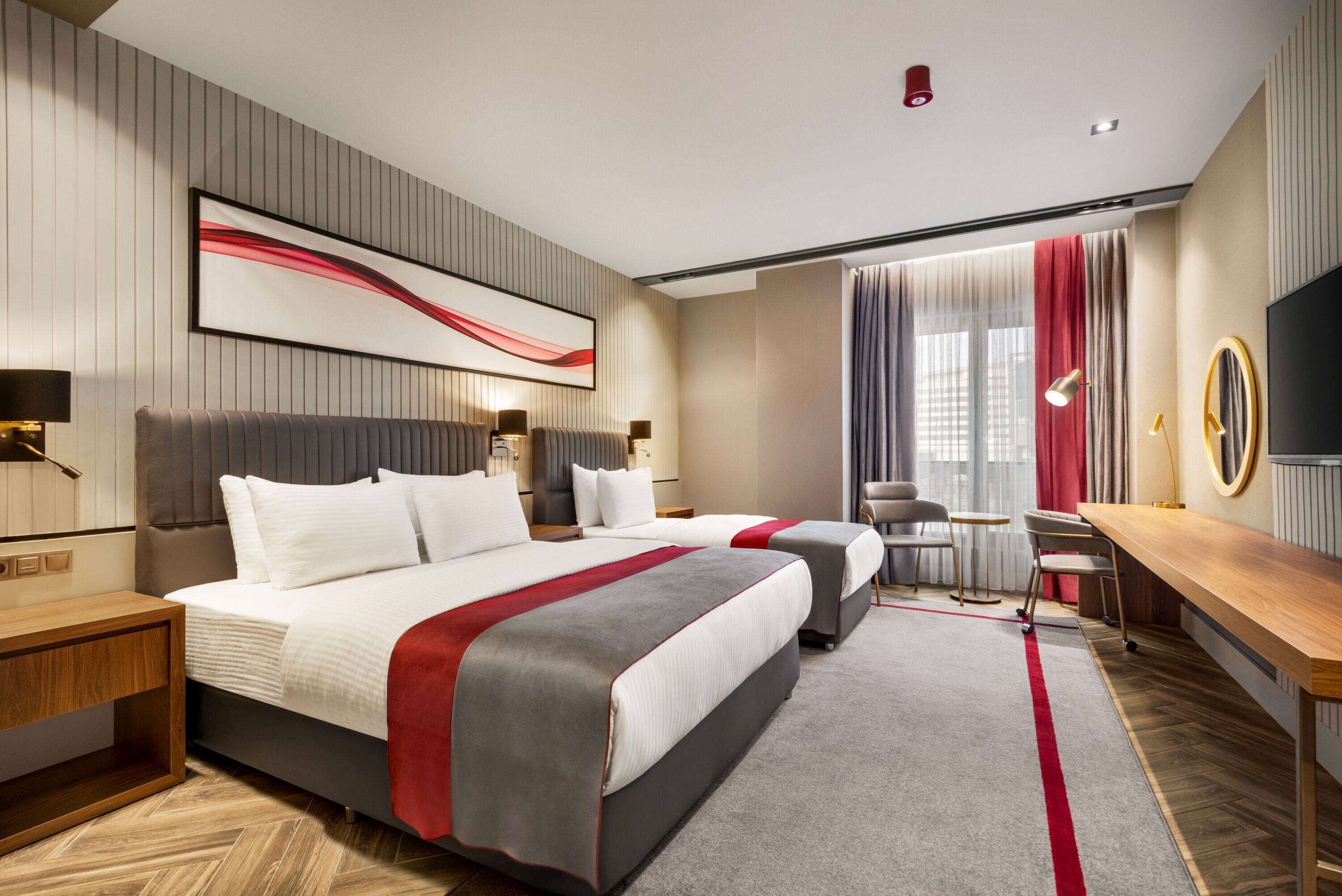A modern hotel room with two beds, a desk, a chair, and a TV.