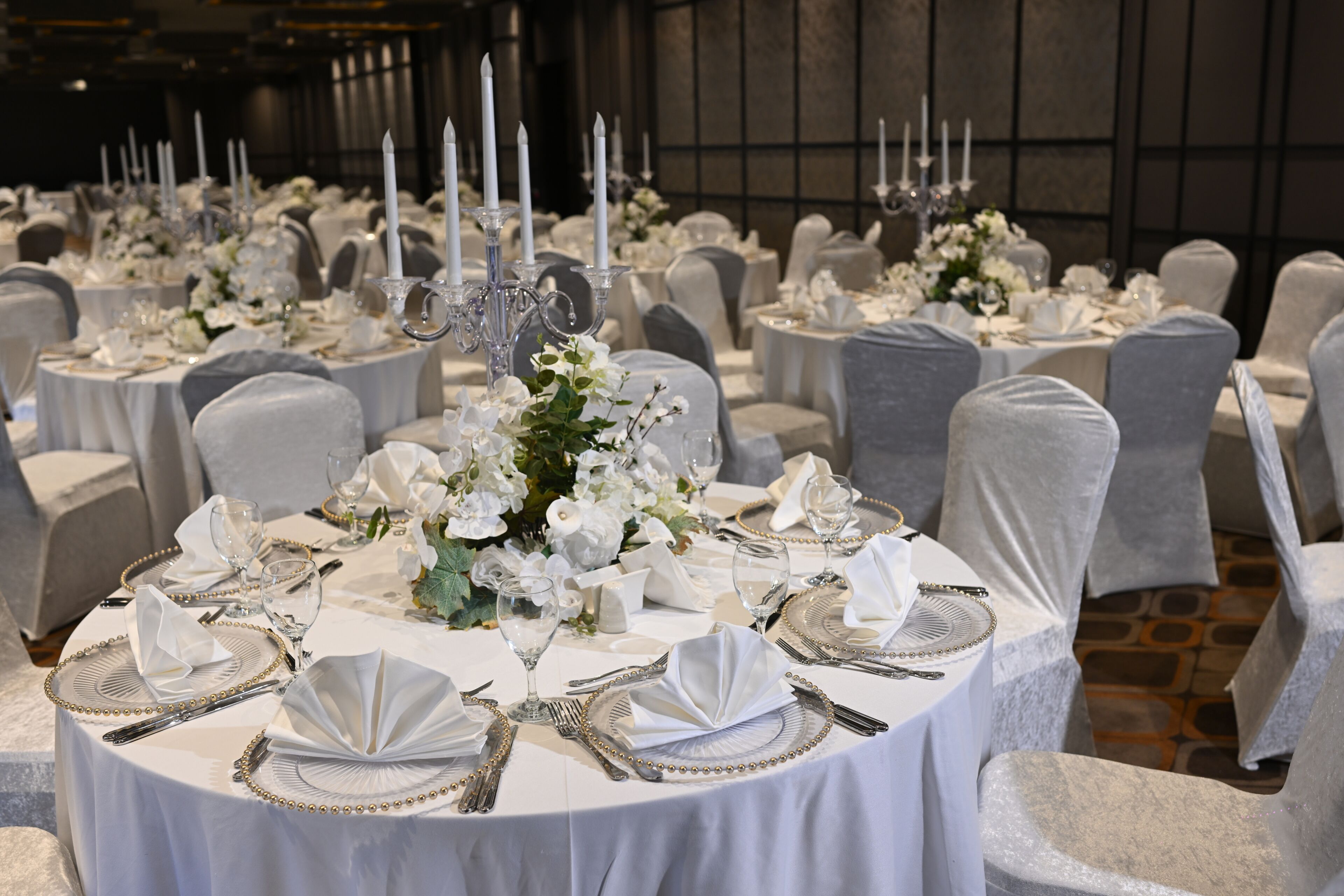 A banquet hall with round tables set for a formal event, featuring white tablecloths, silverware, and floral centerpieces.