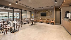 Ein geräumiges Café mit mehreren Sitzbereichen, darunter Tische und Stühle, und einem großen Fernseher an der Wand.