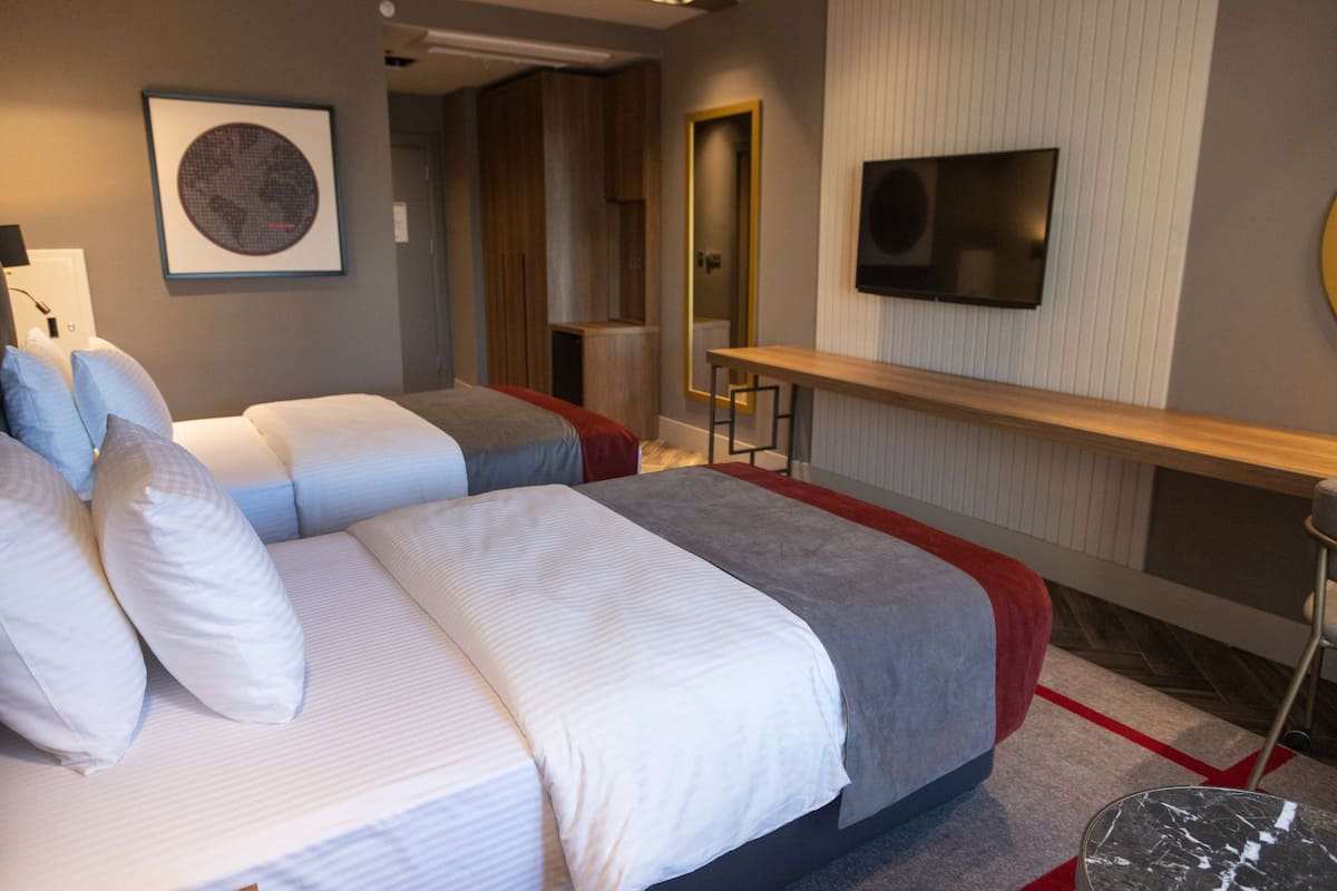 Une chambre d’hôtel avec deux lits, une télévision, un miroir et une petite table.
