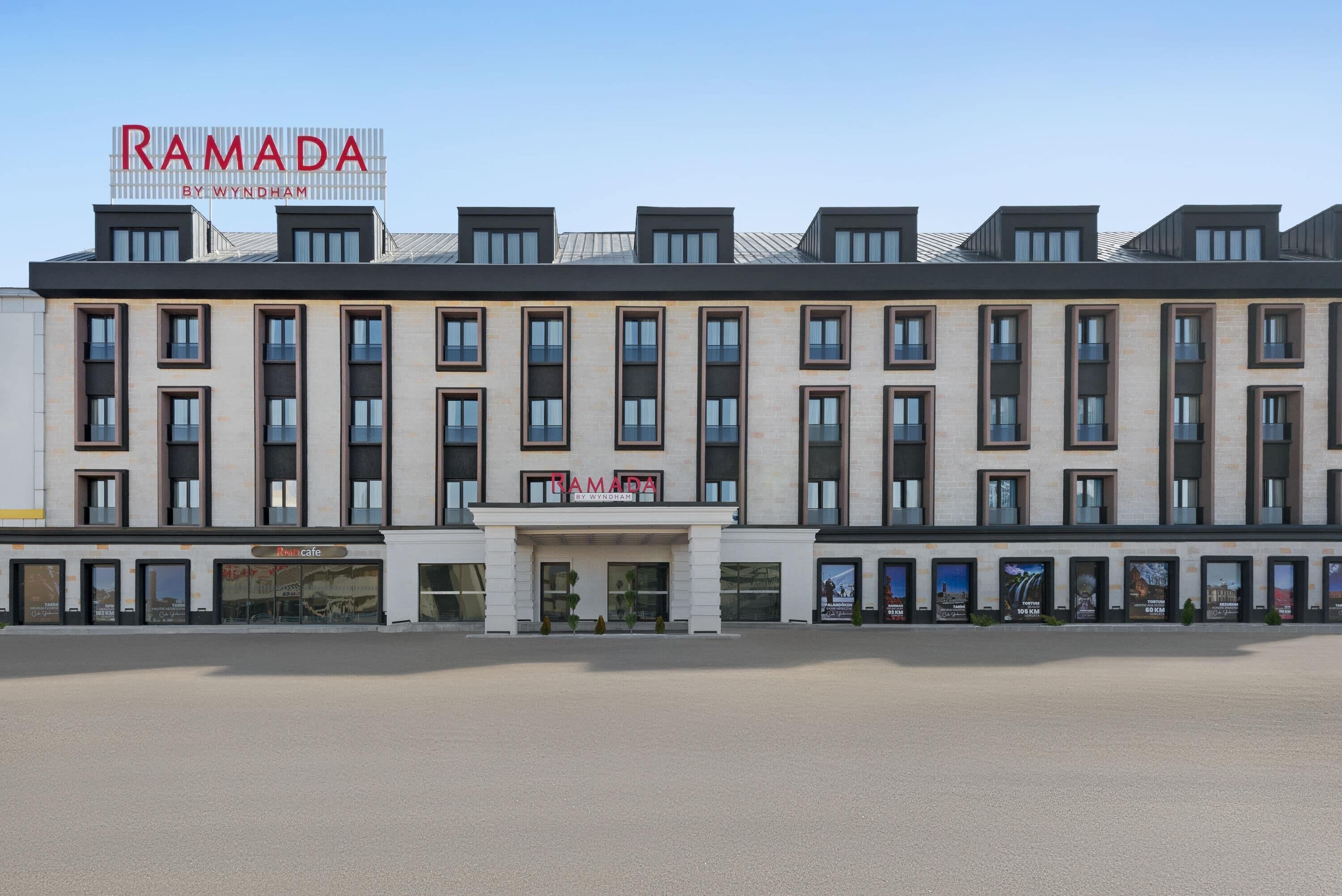 En modern byggnad med en skylt som visar texten ”RAMADA BY WYNDHAM” och ett kafé vid namn ”Ramsgate Cafe” på bottenvåningen.