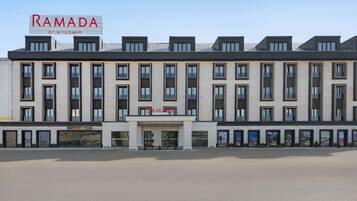En modern byggnad med en skylt som visar texten ”RAMADA BY WYNDHAM” och ett kafé vid namn ”Ramsgate Cafe” på bottenvåningen.
