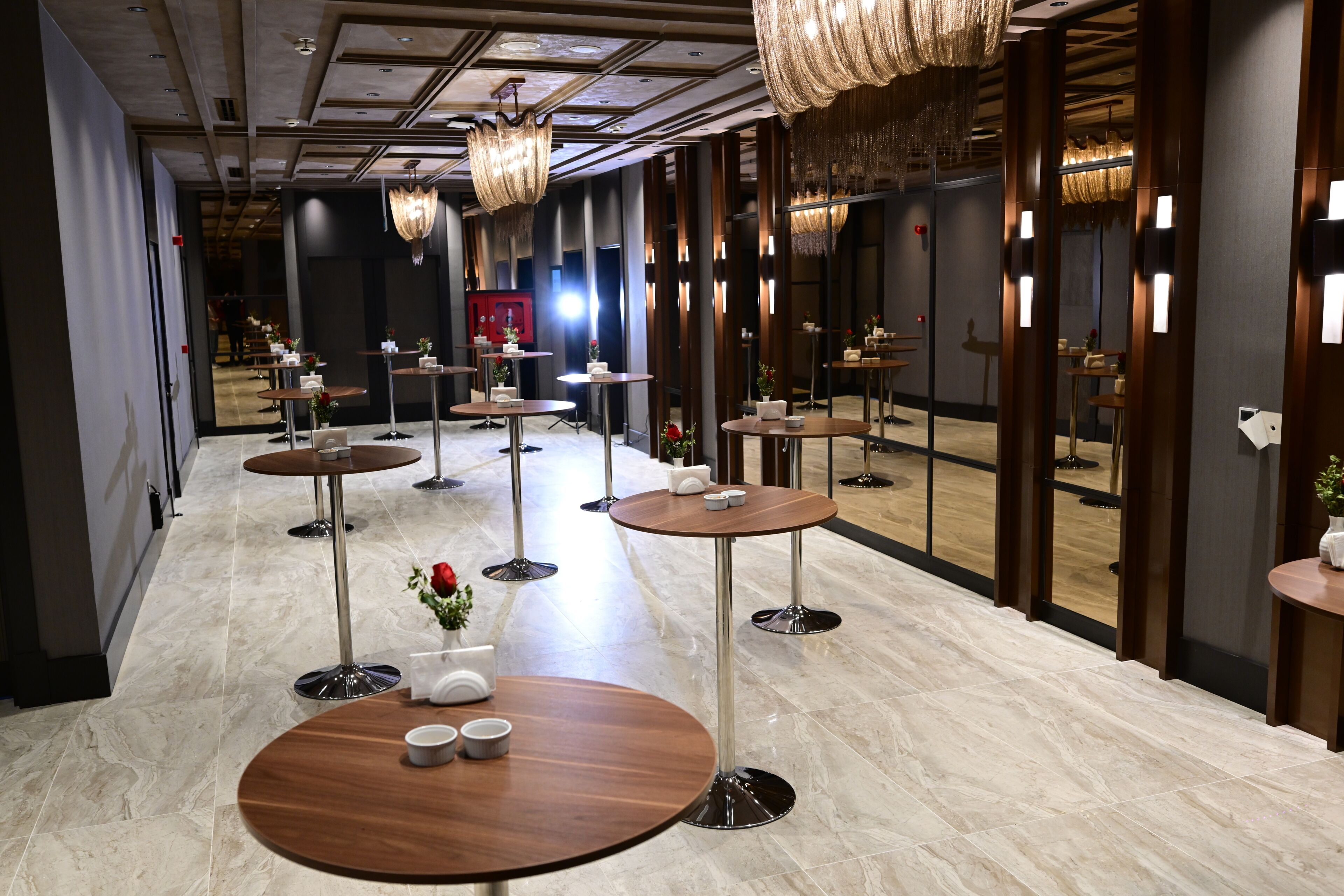 Un vestíbulo de hotel con varias mesas redondas, lámparas modernas y un suelo de mármol pulido.