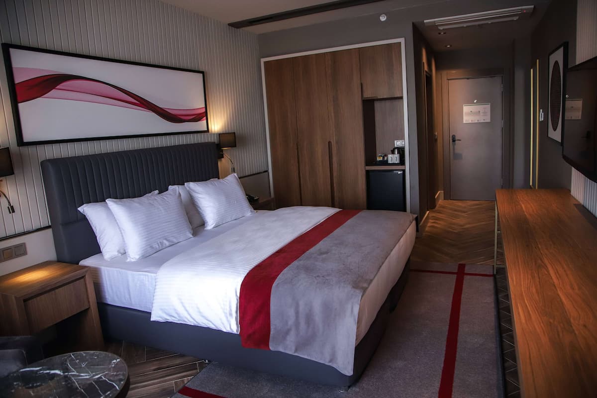 Une chambre d’hôtel moderne avec un grand lit, une armoire en bois, un bureau et un téléviseur fixé au mur.