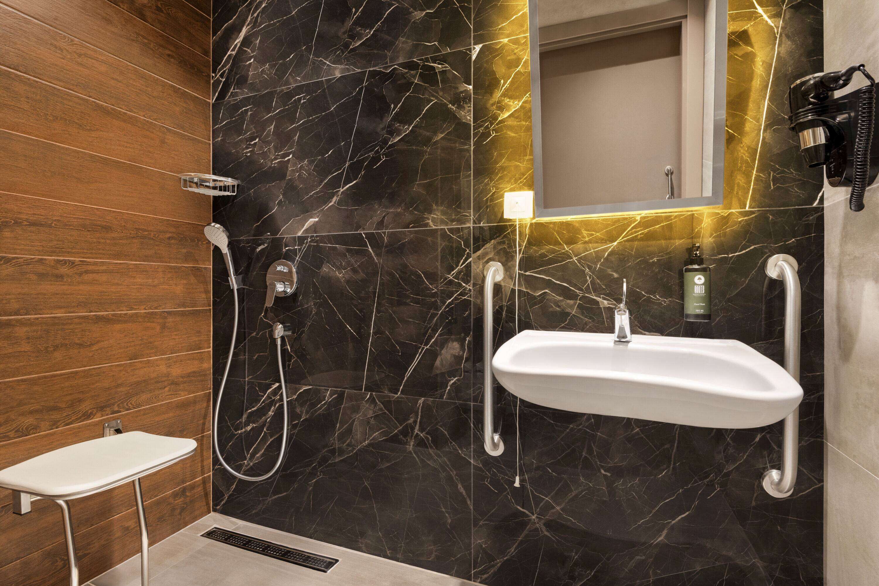 A modern bathroom with a wooden panel wall, a black marble backsplash, a white sink with a mirror, and a handheld showerhead.