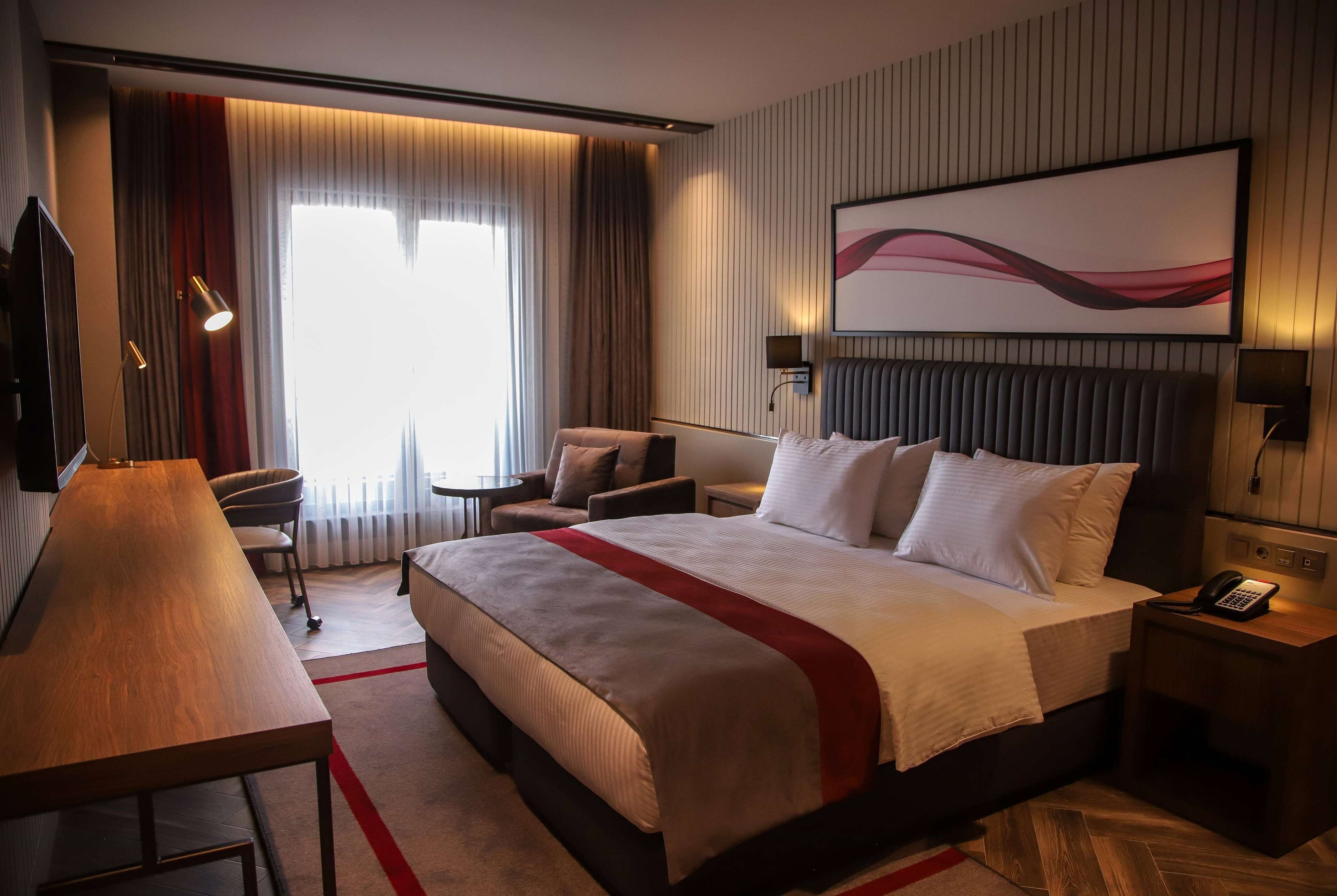 A hotel room with a large bed, a desk, a chair, a TV, and a painting on the wall.